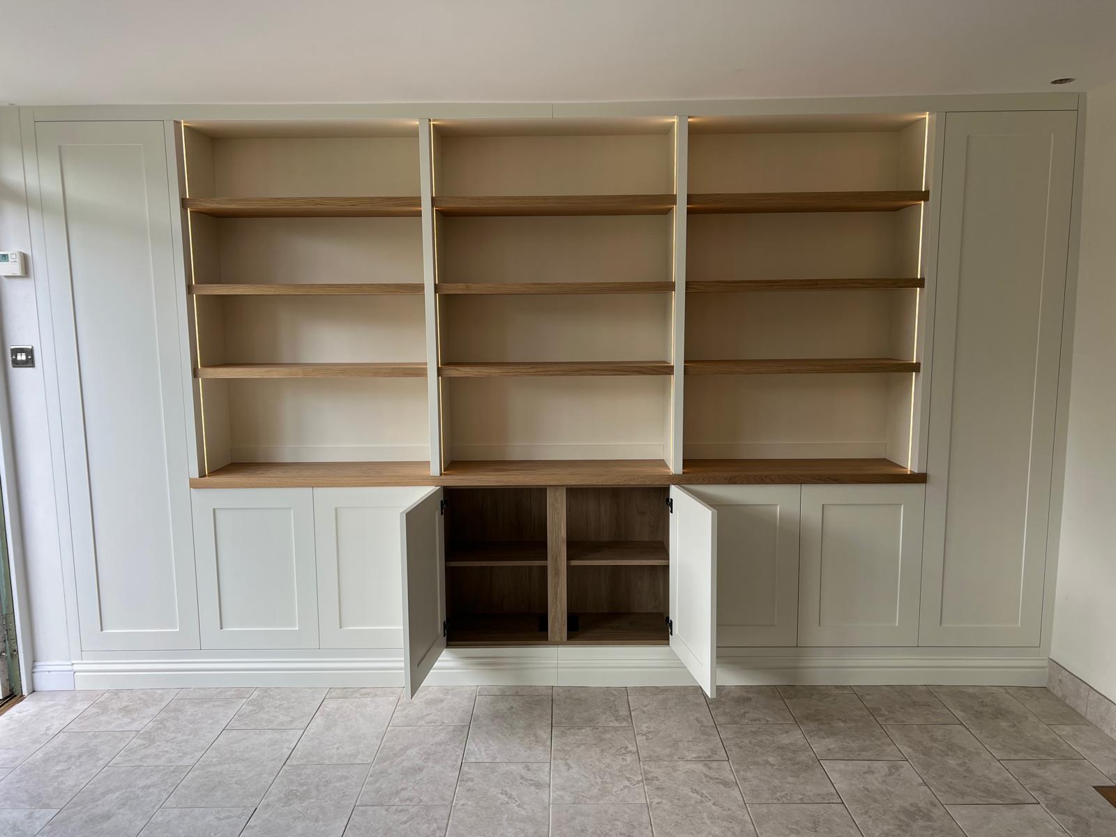 Fitted cream bookcase with oak shelves and panelled base cupboards, doors open to show storage