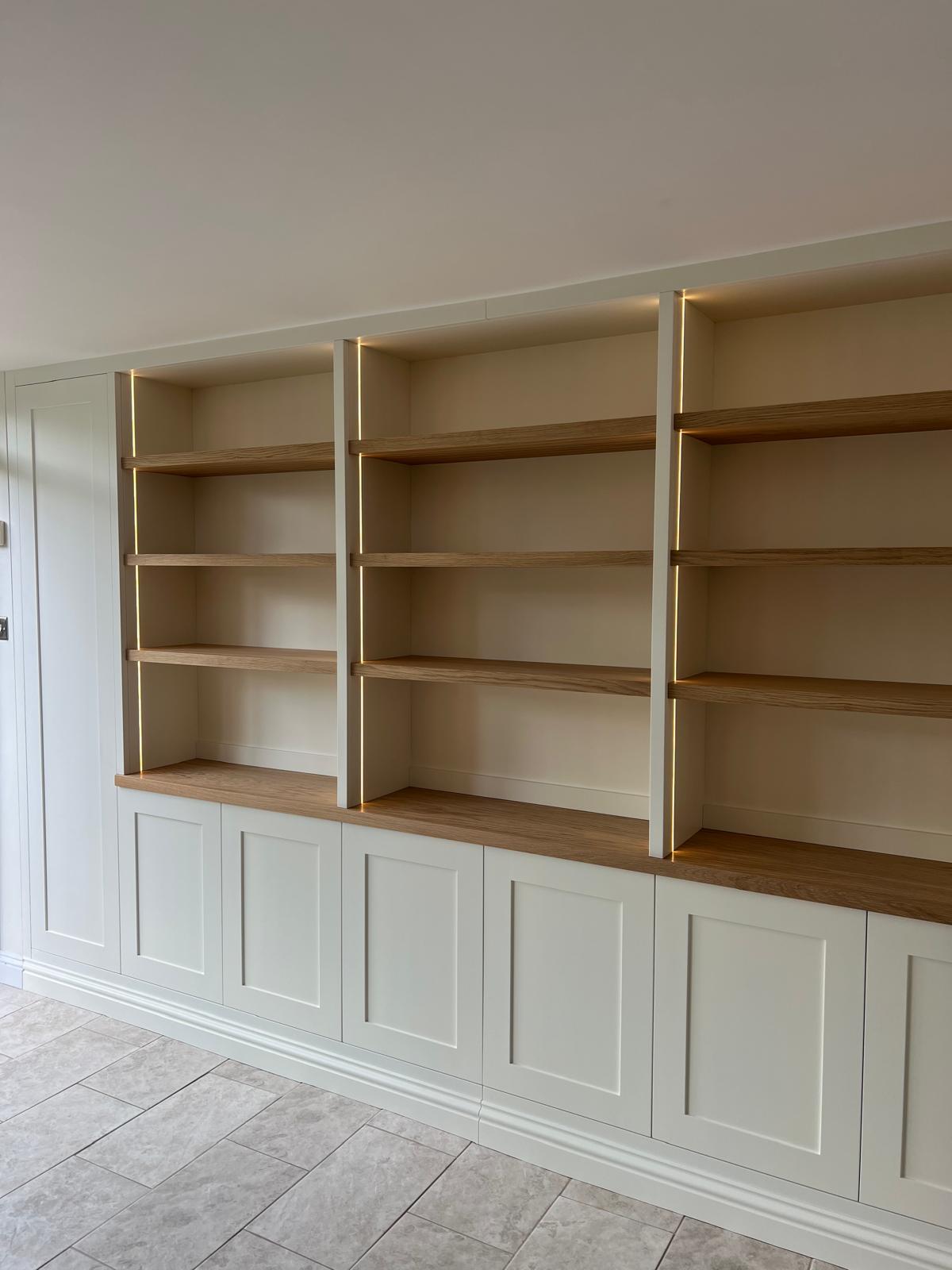 Wide fitted cream bookcase with oak shelves and shaker cupboard base