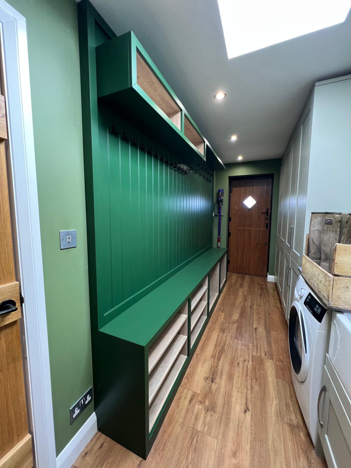 Bespoke green utility and bootroom with panelled walls, drawer storage and integrated appliances